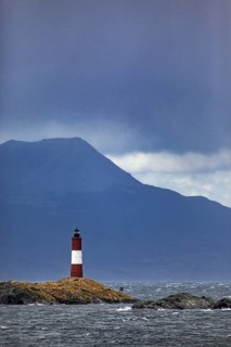 Lighthouse on a rocky island against a mountain backdrop in stormy weather, The lighthouse in the