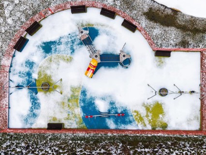 Top-down aerial drone view of a modern children's playground partially covered in snow, featuring