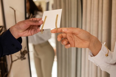 A customer exchanges elegant drop earrings with a sales assistant in a modern, well lit boutique.