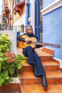 Vertical full length photo of a beauty afro woman playing guitar sitting on stairs outside a