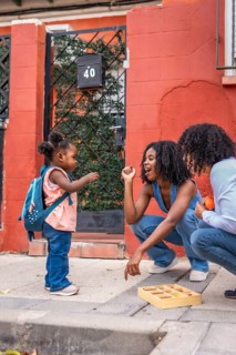 African girl playing with toys with her mother and grandmother outdoors in the city street