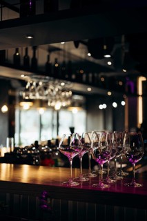 A collection of empty glasses elegantly lined up on a bar counter, illuminated by warm, ambient