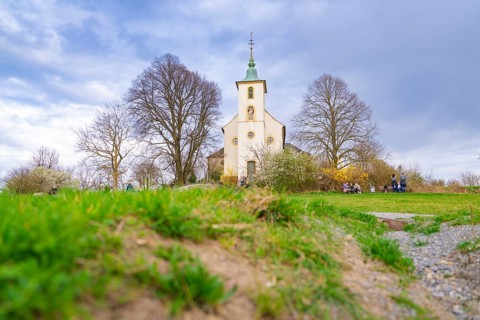 Church surrounded by a green meadow with bare trees and a cloudy sky. Spring-like atmosphere,