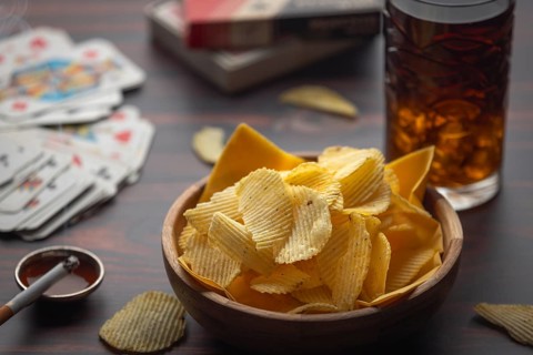 Bowl with chips, playing cards and cigarette next to drink on a table