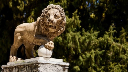 Lion statue on pedestal in front of a background of trees, Rodini Park, City Park, Rhodes Town,