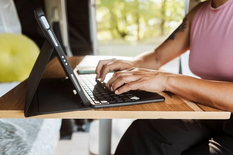 A woman works from her laptop inside a van set against a backdrop of colorful autumn foliage in New