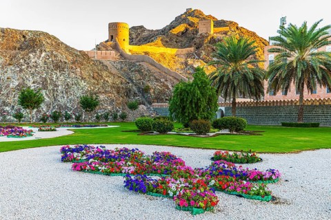 Park with gravel paths, flowers and palm trees at the Sultan's Palace, behind the city wall with
