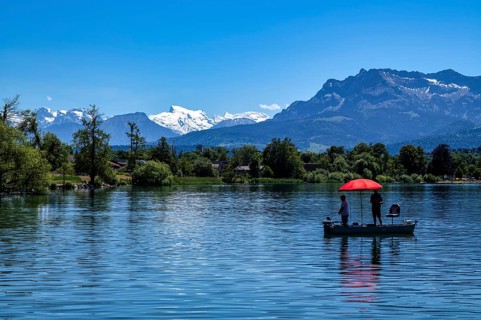 Angler auf Boot, Sonnenschirm, rot, im Hintergrund Schweizer Alpen, Titlis, Pilatus, Sempachersee,
