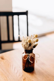 A glass vase tied with twine holds a bouquet of dried flowers, set on a wooden table in a cafe.