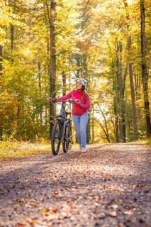 Woman pushing ebike through autumn forest, Black Forest, Gechingen, Germany