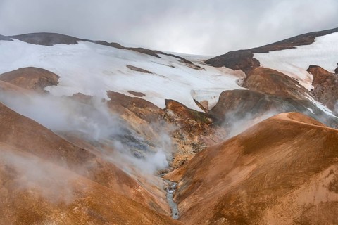 Steaming stream between colourful rhyolite mountains and snowfields, Hveradalir geothermal area,