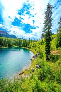 Alpine scenery reflecting on turquoise waters of karersee lake under a cloudy blue sky, surrounded