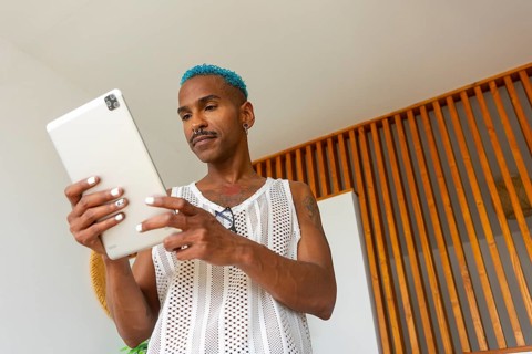 An LGBTQIA+ man embraces the holiday spirit, engaging with a tablet in a warm, inviting setting. A