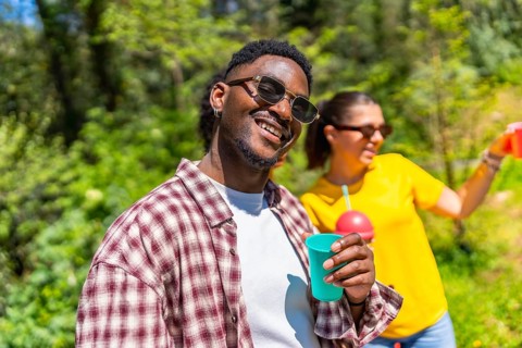 Young man smiling and holding a refreshing drink on a sunny day, enjoying the company of friends in