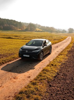 A car on a country lane, flanked by green fields in the early morning light, electric car VW ID5,