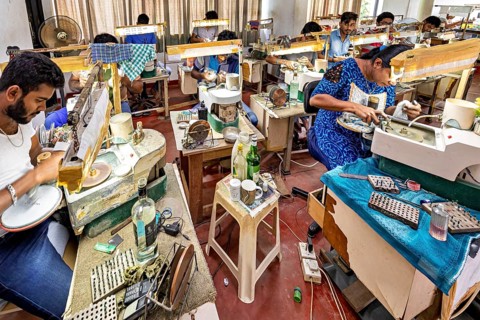 Several people work on machines in a busy, creative workshop environment. The sapphire and gemstone