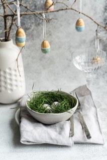 An elegantly set Easter table featuring a bowl of eggs nestled in fresh green grass, accompanied by