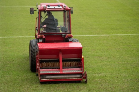 A man in a tractor with a disc seeder drill sowing grass on a football field in Lubin, Poland