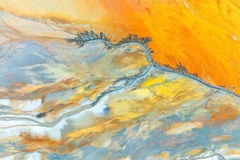 This aerial view captures intricate fractal mud patterns with vibrant orange and blue hues,