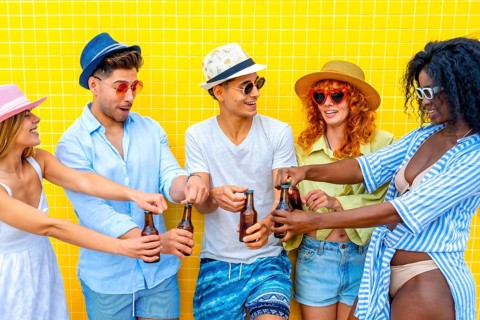 Group of cheerful multi ethnic friends wearing summer clothes and hats toasting with beer bottles