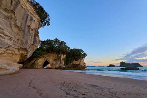 View of a cave on the beach, the sea and a softly coloured sunrise, Cathedral Cove, Coromandel,