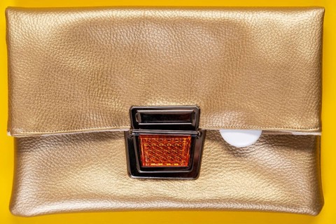 An Apple Air tag lies on a golden faux leather clutch against a plain yellow background