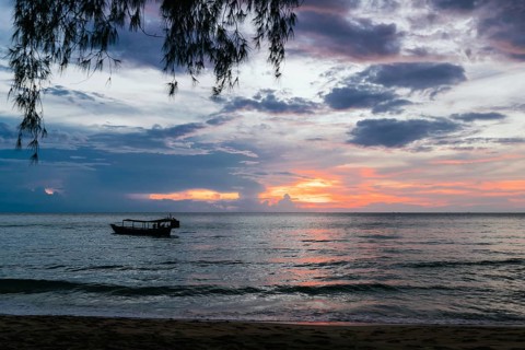 A serene sunset over Koh Rong Island, Cambodia, with vibrant orange and purple hues reflecting in