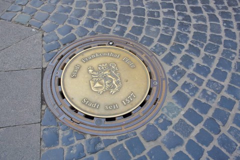 Round manhole cover with city coat of arms and date 1577 for granting city rights, inscription,