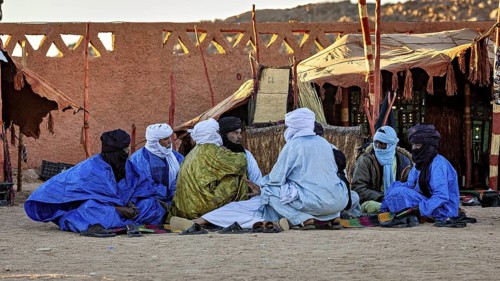 Group of people in traditional dress sitting in front of a tent in the desert, men at the