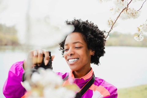 A joyful Black woman photographer, in an outdoor setting, capturing the delicate beauty of cherry