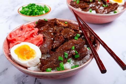 Gyudon Japanese beef with rice, pickled ginger, boiled egg slice, garnished with green onions, in a