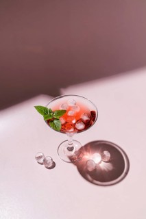 A refreshing pink cocktail adorned with basil leaves, served in a stylish glass with glistening ice