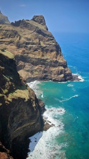 High cliffs with lush vegetation above the turquoise sea under clear skies, hiking, Santo Antao,