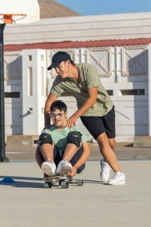 A joyful scene of a teenager with Down syndrome skating with the support of his brother The