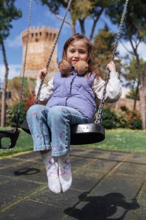 A young girl joyfully swings at a playground with a historical tower in the background, symbolizing