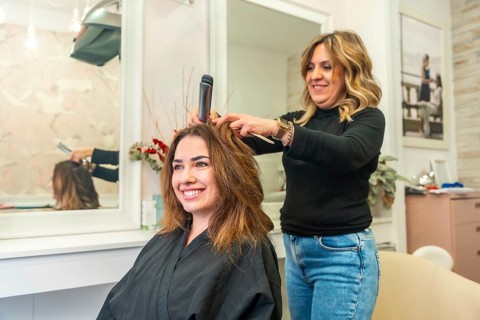 Hairdresser styling smiling client's long brown hair with a flat iron in a bright beauty salon,