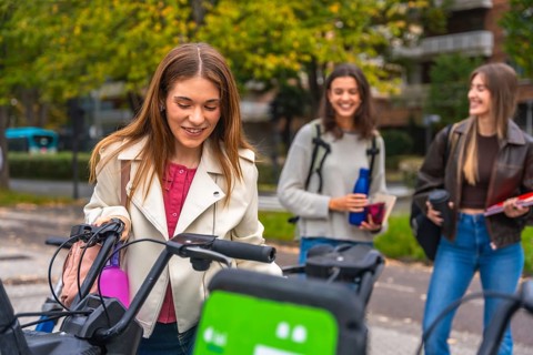 Young college women engaging in sustainable urban travel, renting bicycles from a sharing station,