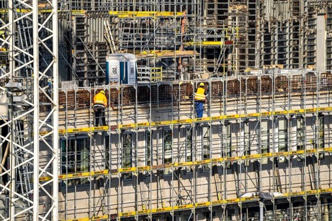 Large construction site, scaffolded new building, factory and office building, workers on the