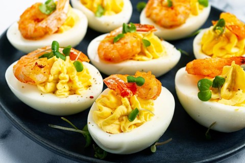 Boiled eggs stuffed with yolk and seasoned with mayonnaise, stuffed eggs with shrimp, on a black