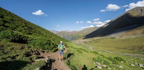 Mountaineers on a hiking trail, green high valley with mountain stream, Keldike Valley on the way