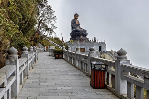 A long walkway leads to an imposing Buddha statue in a peaceful temple complex, The Buddha statues