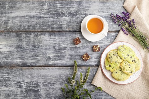 Green cookies with chocolate and mint on ceramic plate with cup of green tea and linen textile on