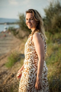 A woman smiles warmly while standing near the beach in Italy. The golden sunlight illuminates her