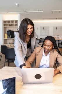 Two businesswomen collaborating on a laptop, enjoying a productive moment during their business