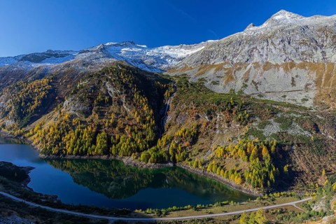 The Galgenbichl reservoir with a mountain forest in fall foliage on a bright sunny morning. Seen