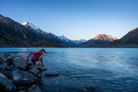 A woman on a rock at Tasman Lake. On the left, Mount Cook. Golden hour. Aoraki Mount Cook National