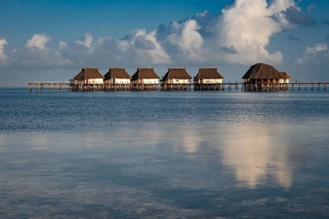 Luxury thatched roof bungalows built over the calm turquoise water of the Indian Ocean with a