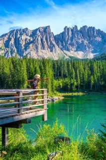 Tourist with open arms enjoying the breathtaking view of lake carezza and latemar mountain range,