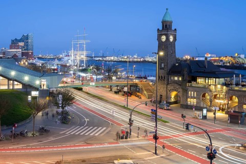 Piers with subway station and light strips of vehicles in the foreground with sailing ship Rickmers
