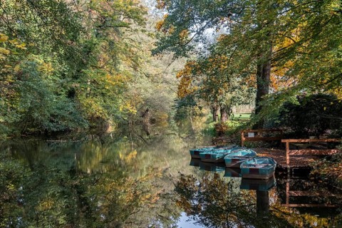 Quiet river with reflecting trees and resting boat in autumn, Ahaus-Alstätte, Münsterland, North